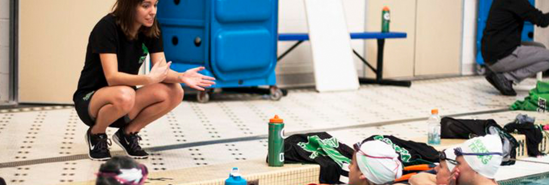 Swimming Coach discussing performance techniques with athlete swimmers in pool