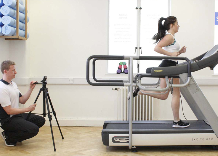 Physiotherapist recording running techniques of athlete on treadmill